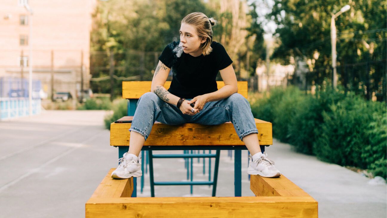 A young person vaping on a bench outside. 