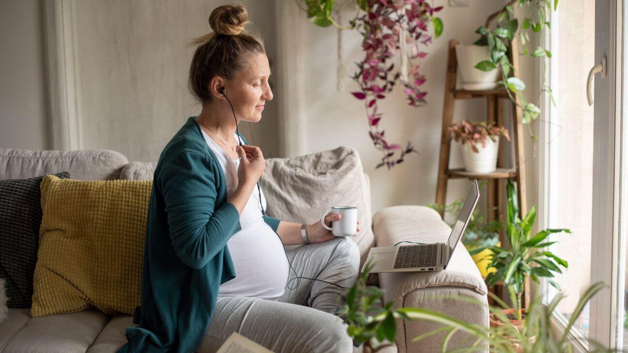 pregnant woman sitting in front of window and looking at her laptop