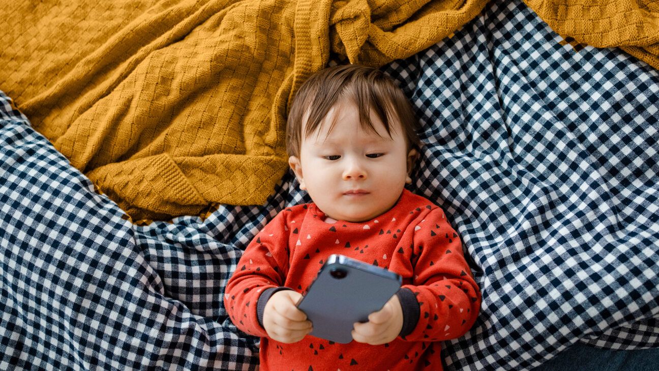 An infant with a phone on a bed.