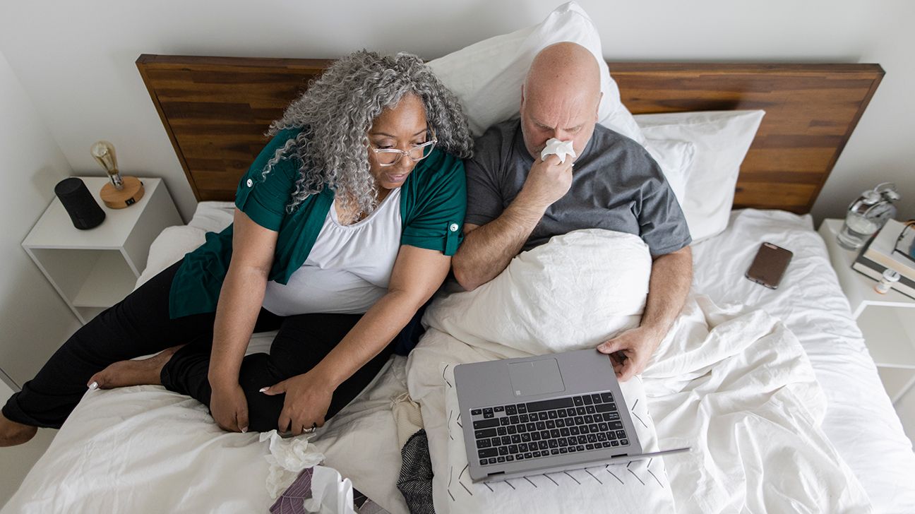 man in bed with cold on laptop