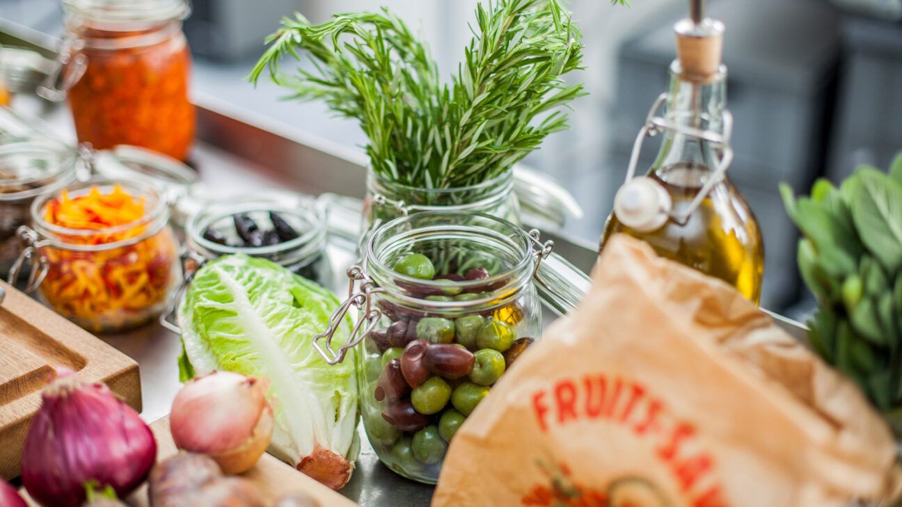 Foods including olives lettuce and herbs are seen on a counter.