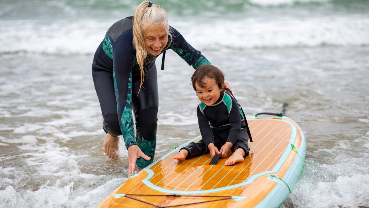 A woman pushes a child on a surf board.