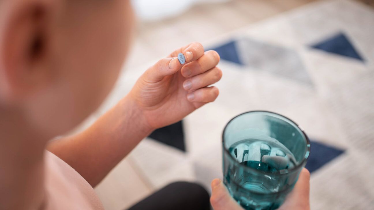 A person holds a pill and glass of water.