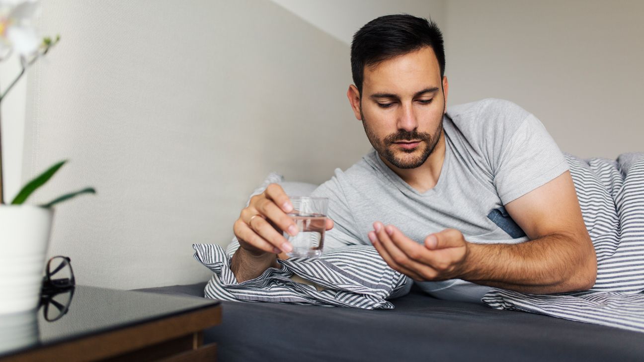 A man lying on a bed taking medication.