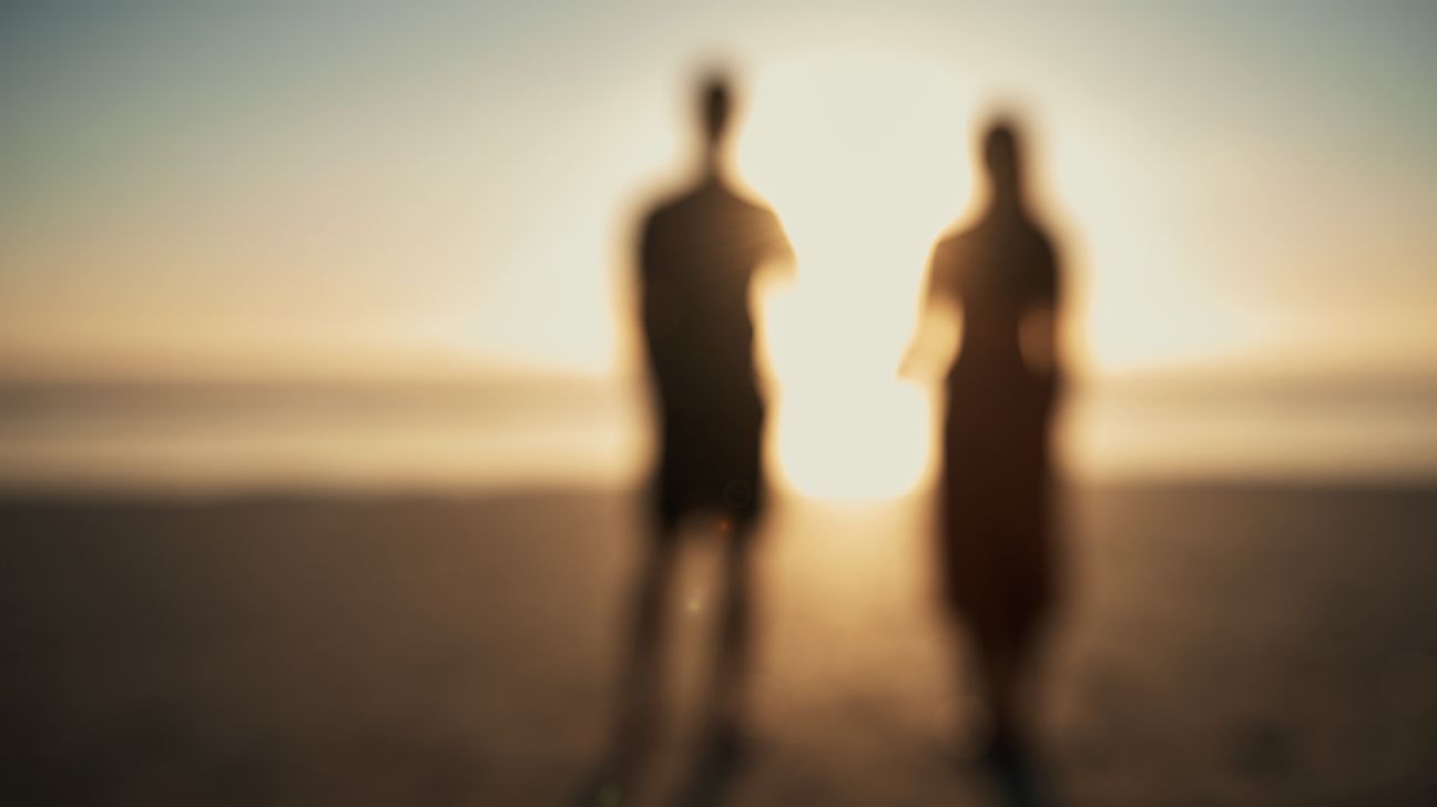 شخصيتان ضبابيتان لأشخاص يقفون على الشاطئ عند شروق الشمس
