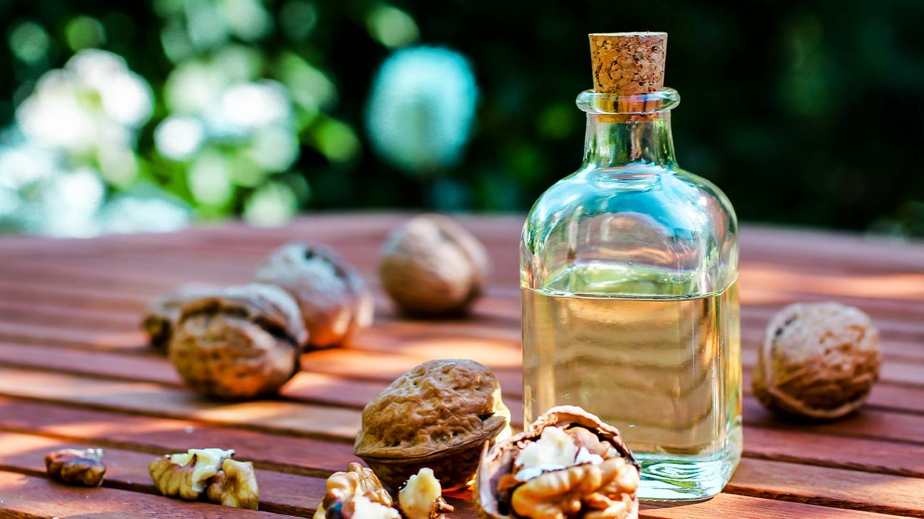 A corked glass bottle of walnut oil with walnuts beside it on a wooden table