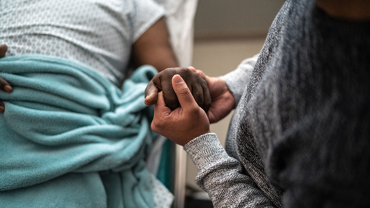 En sykepleier som holder hånden til en med hjertesvikt i sluttstadiet. 
