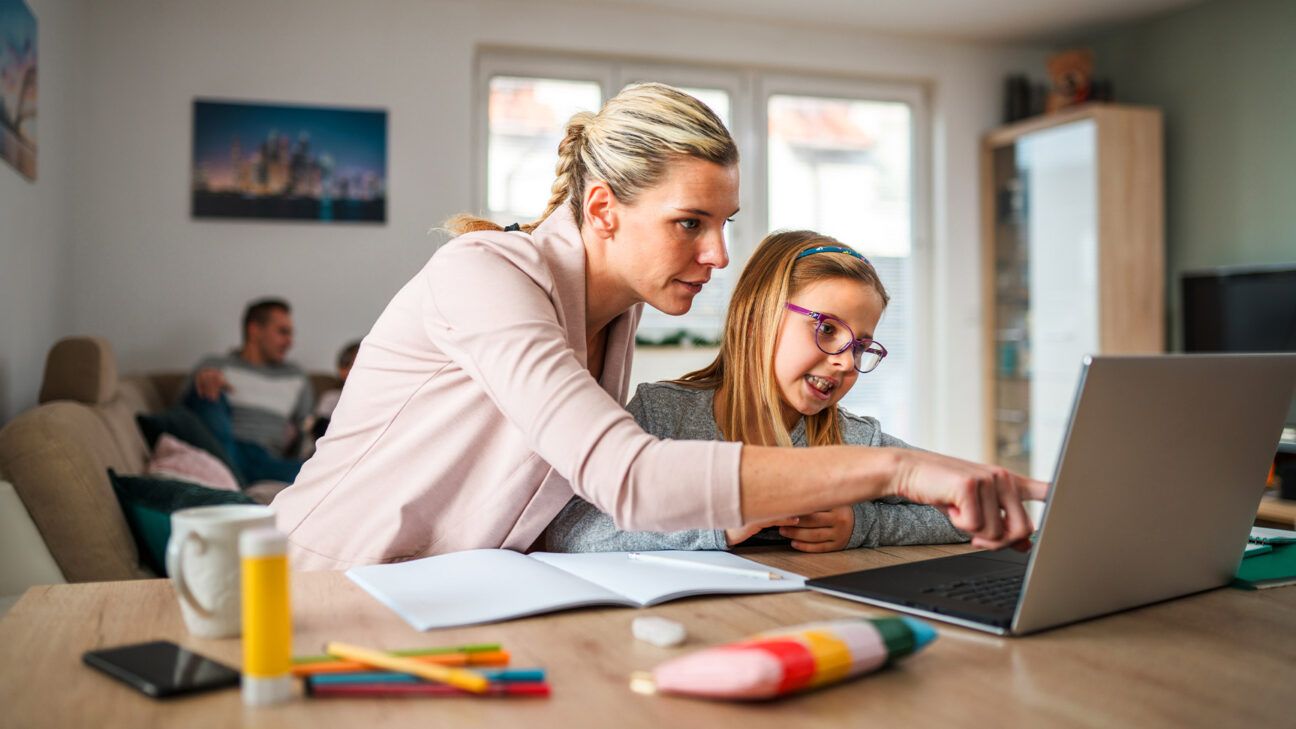 A mother helps her daughter with homework on a computer.