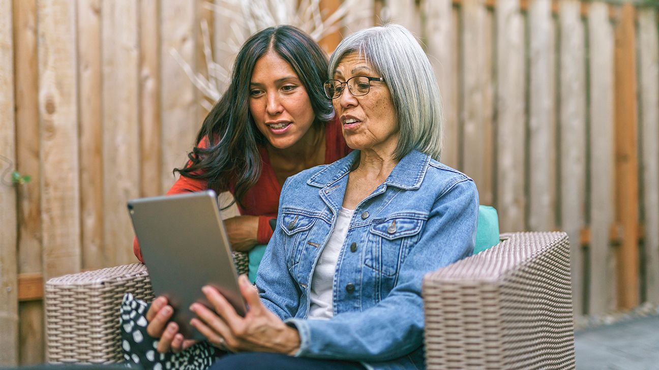 Femeie în vârstă care se uită la tabletă digitală cu fiica adultă