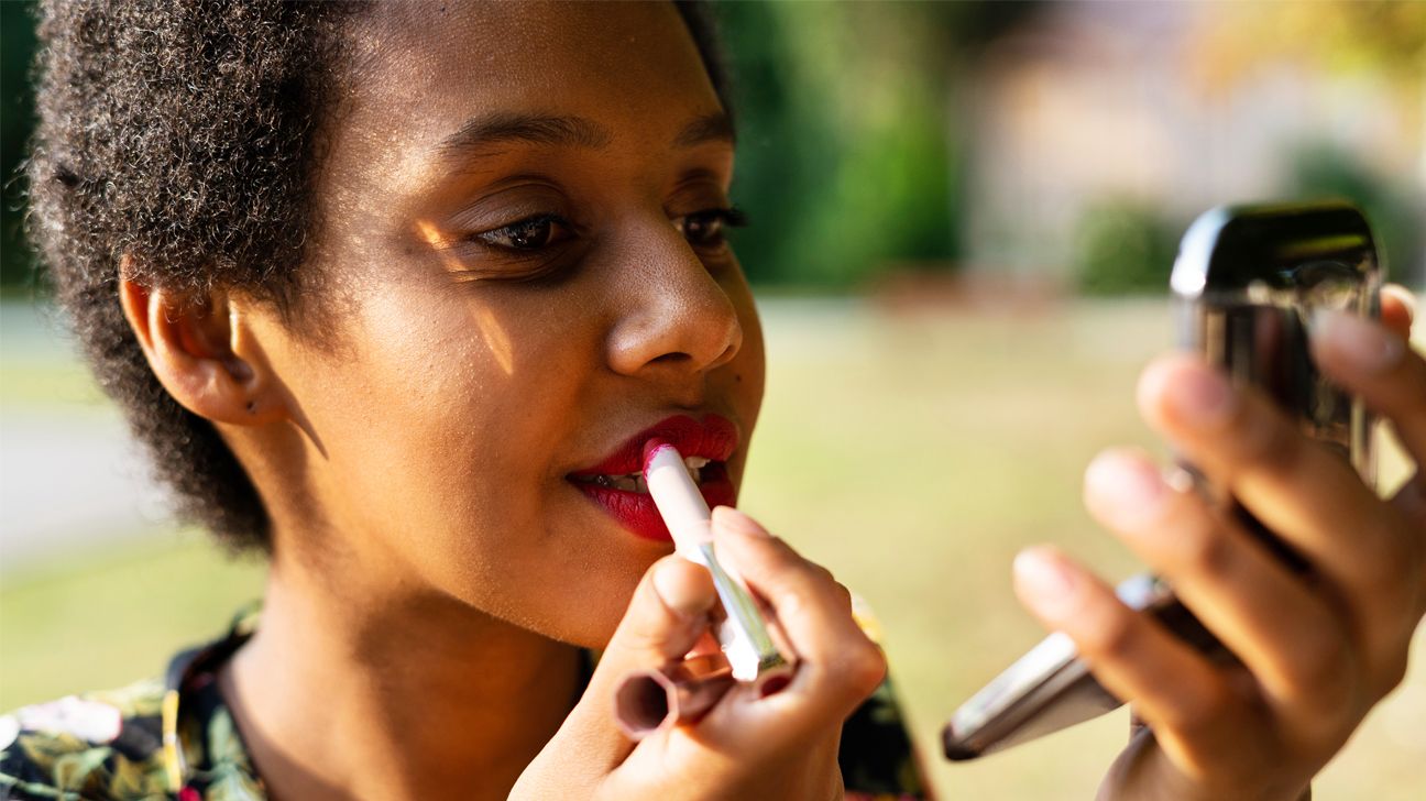 A woman applies lipstick while outside.