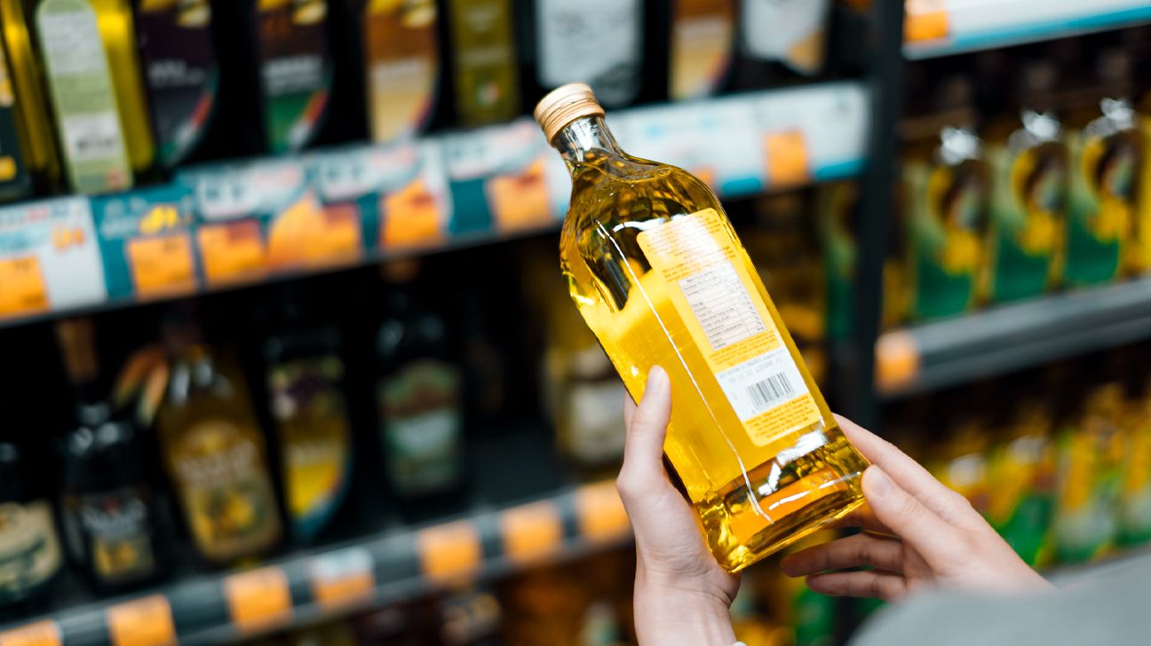 Close up of young woman grocery shopping in a supermarket. Standing by the aisle, holding a bottle of organic cooking oil, reading the nutritional label and checking ingredients at the back