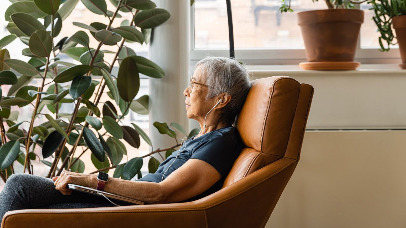 older person with multiple myeloma wearing earbuds, sitting, and looking out a window