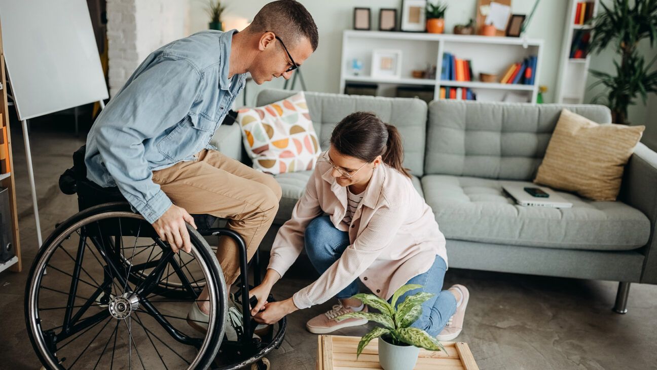 شخص يساعد زوجته المصابة بمرض التصلب الجانبي الضموري (ALS) في الجلوس على كرسي متحرك