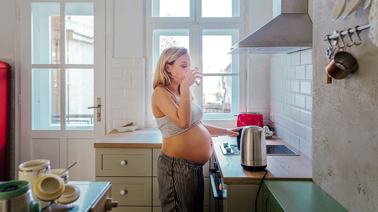 المرأة الحامل في المطبخ تشرب الماء