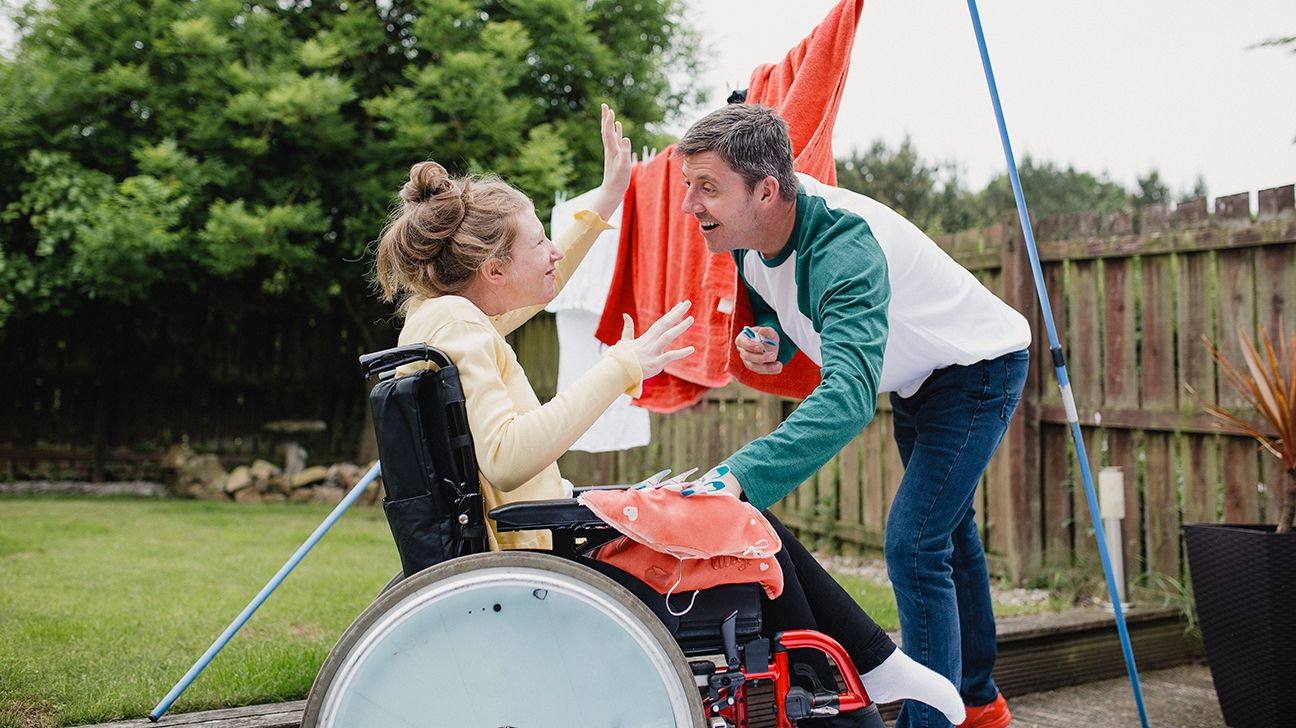 father helps his daughter with juvenile ALS hang laundry outside to dry