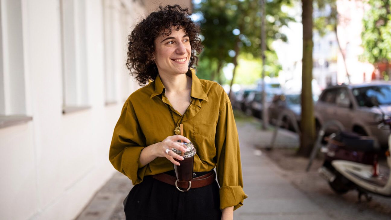 A woman drinks coffee while walking on a sidewalk.