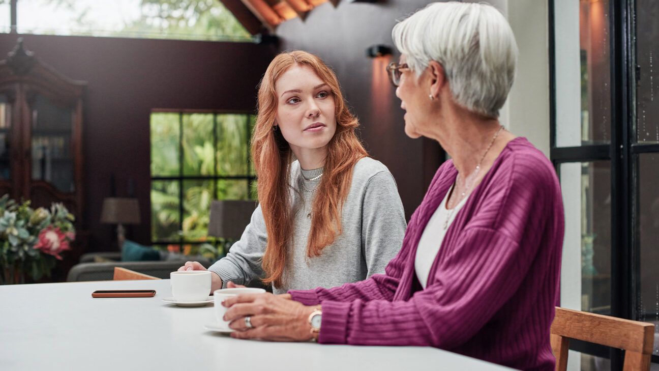 Two women are seen talking at a table.