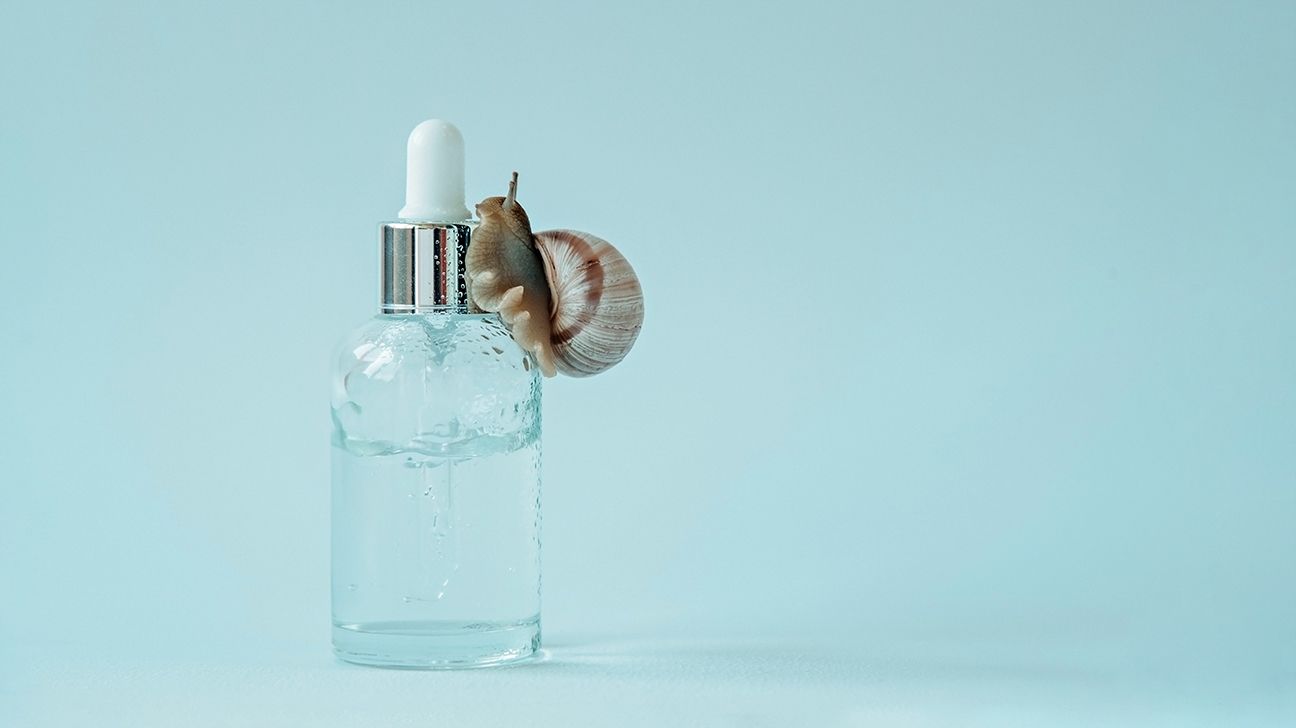A snail crawling on a vial of skin care serum.