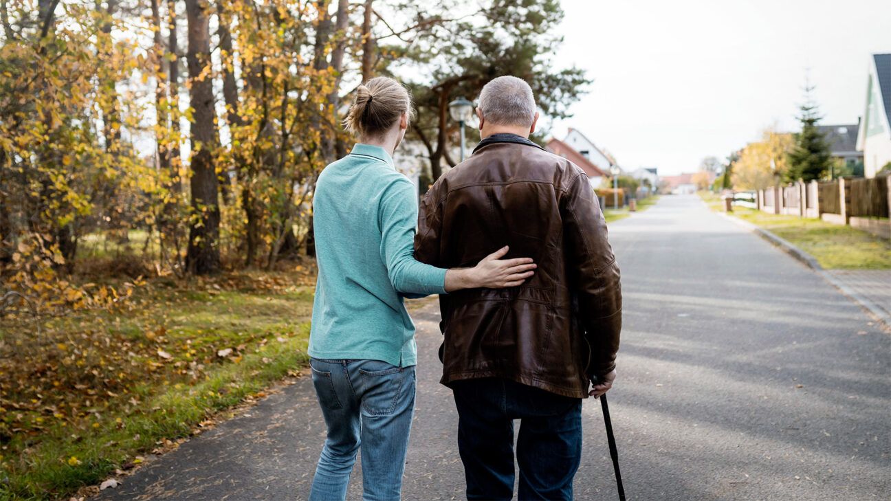 A person helps another person with a can walk down a street.