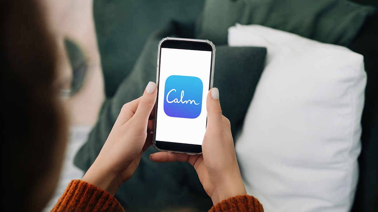 person holding a smartphone with a white screen facing them (and you, the reader). in the middle of the white screen is a blue app that says 'calm'