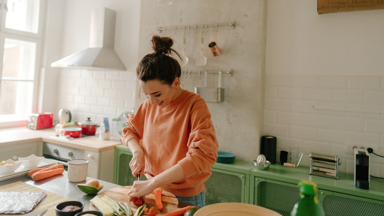 Egy fiatal nő zöldséget aprít az ételhez a konyhájában. 