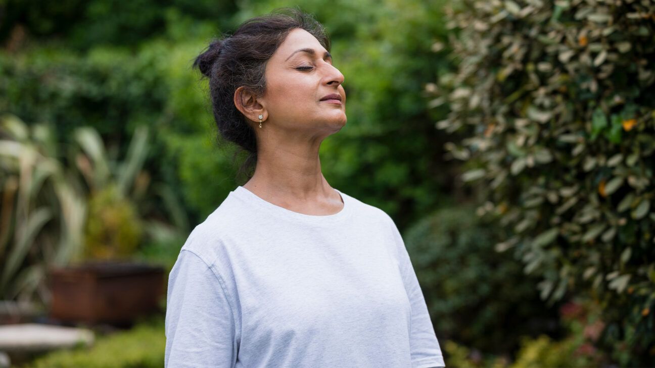 Woman in white shirt outside with her eyes closed.