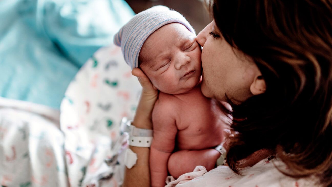 A mother kisses a newborn baby in a hospital bed