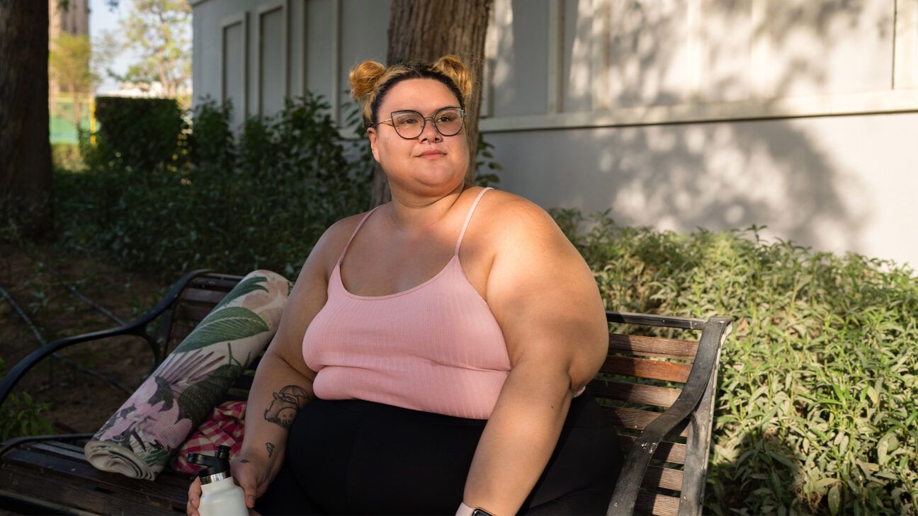 A woman in a pink tank top sits outside on a bench.