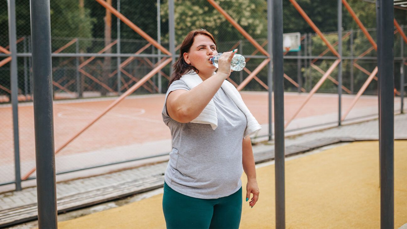 A woman drinks from a water bottle at an outdoor basketball court