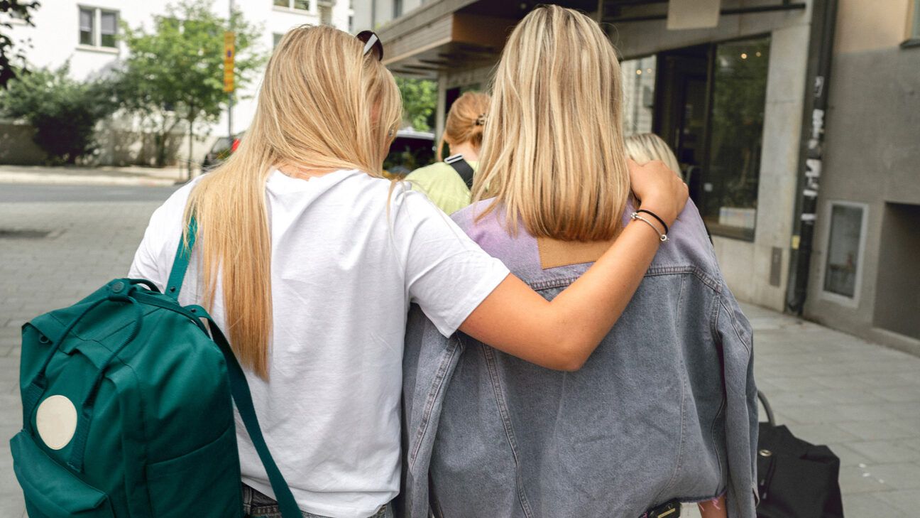 A teenage girl puts her arm around another teenage girl as they walk together