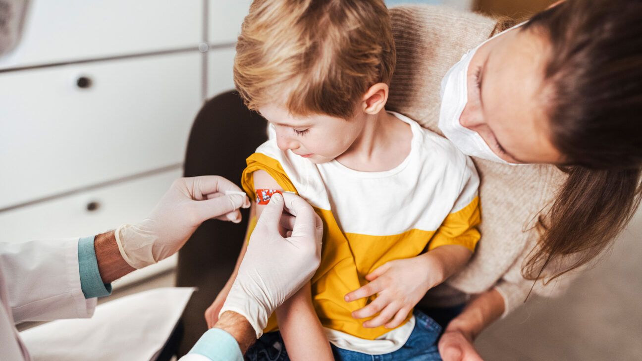 Child in yellow and white shirt gets bandaid after vaccine.