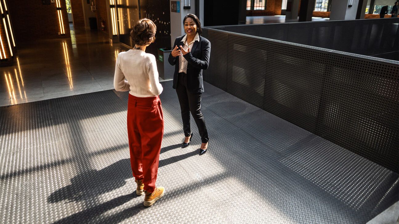 Two women stand and talk in an office.