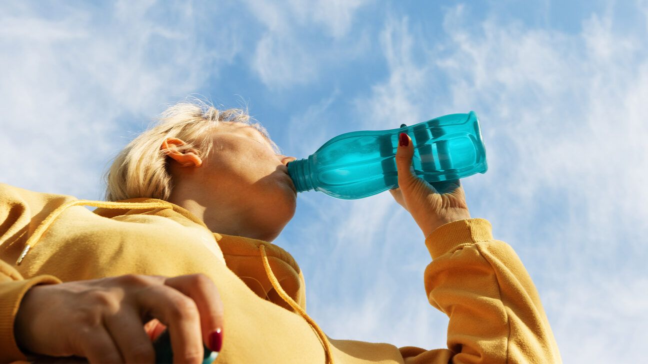 A person drinks from a blue plastic water bottle.