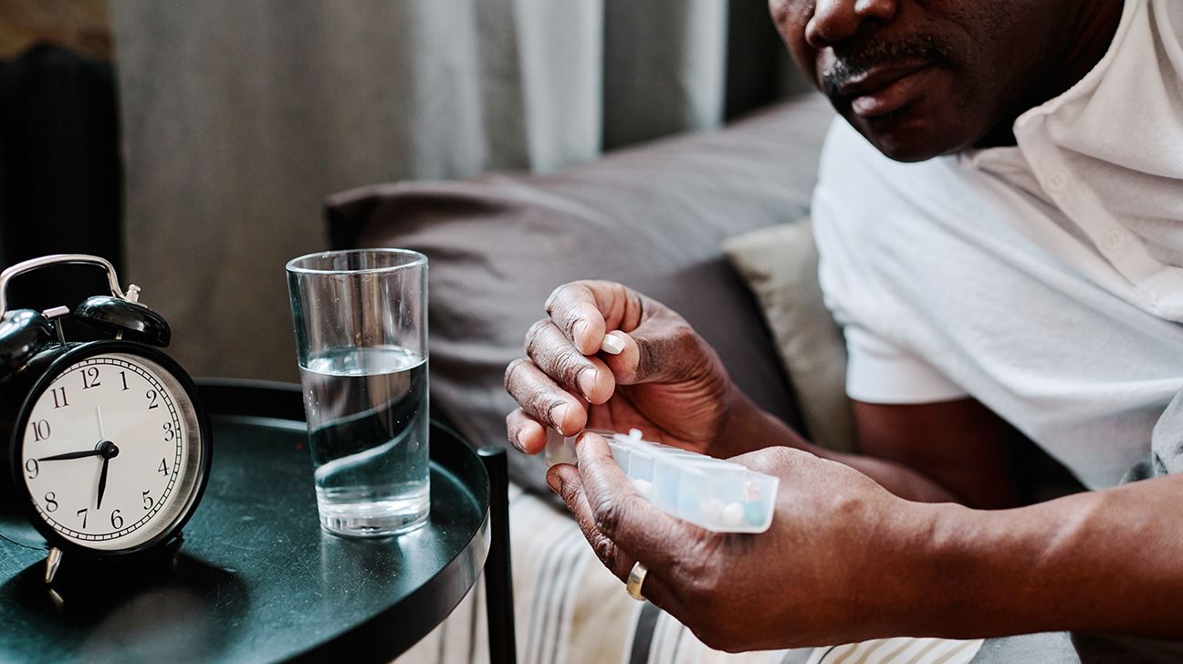 A man takes pills while sitting on his bed.