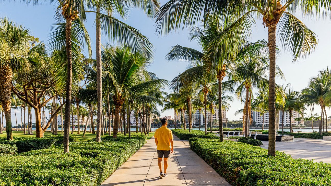 Man in orange shirt and black shorts walks down sidewalk in Miami.