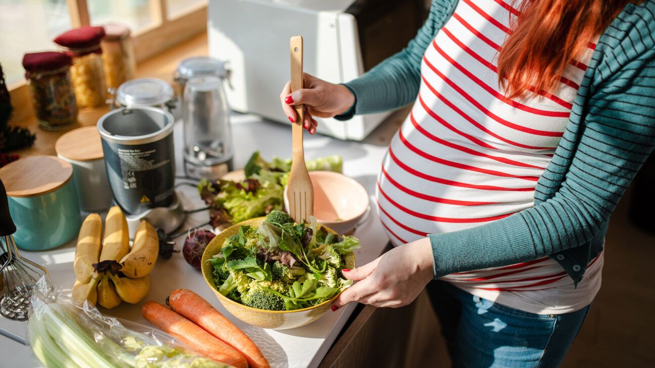 A pregnant woman in a striped shirt eats a salad.