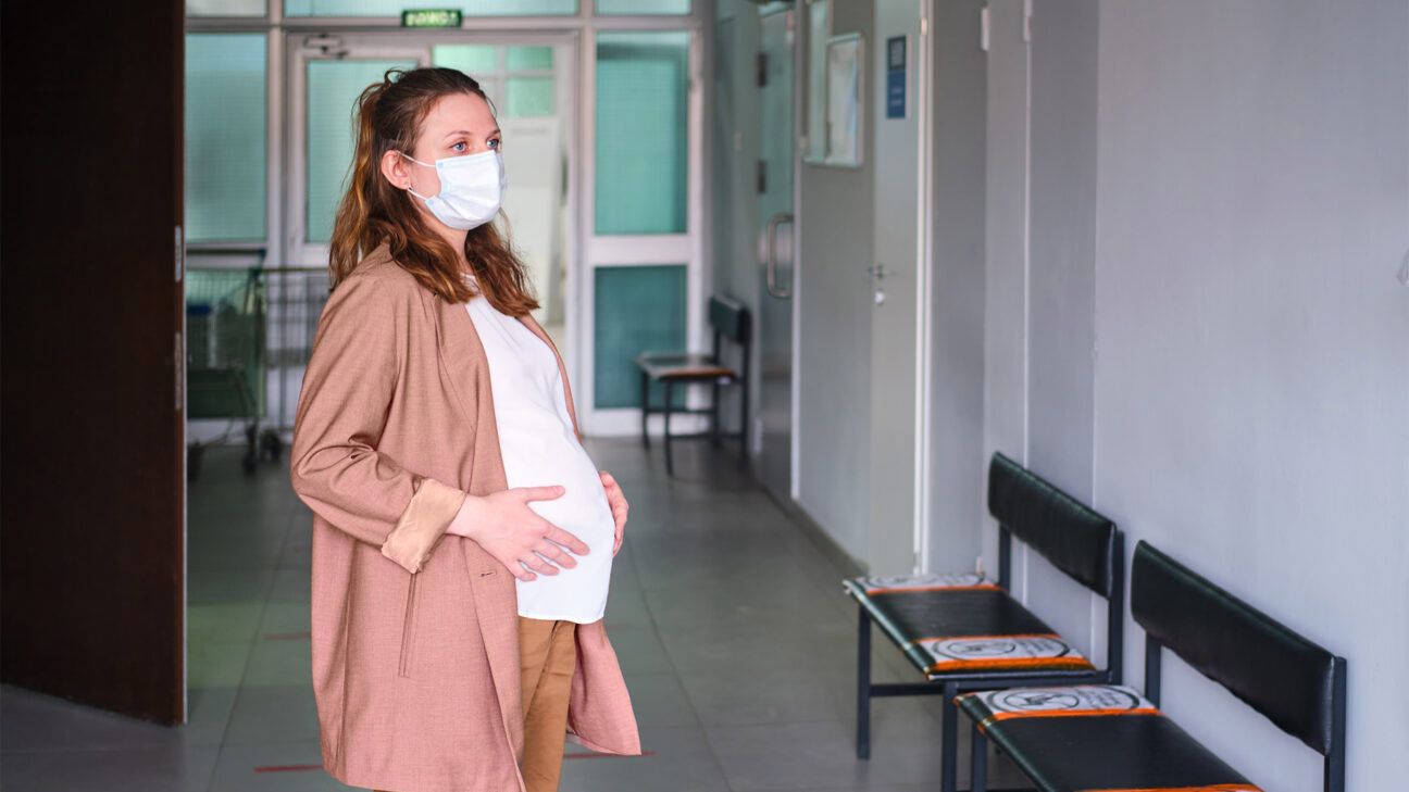 Pregnant woman in a white shirt stands in a hallway.