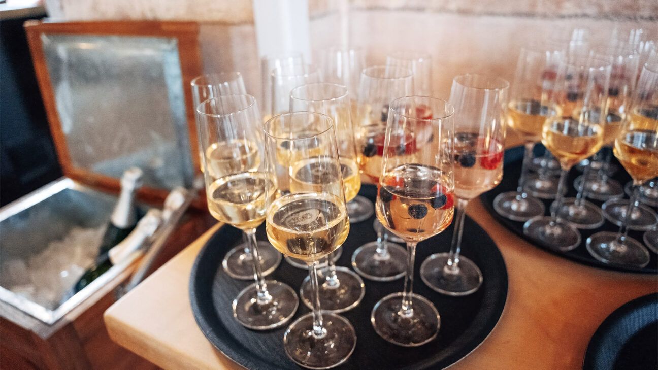 A tray of white wine glasses is seen on a table.