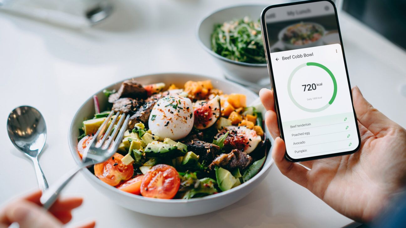 Large salad and someone holding a mobile phone showing a calorie tracking app