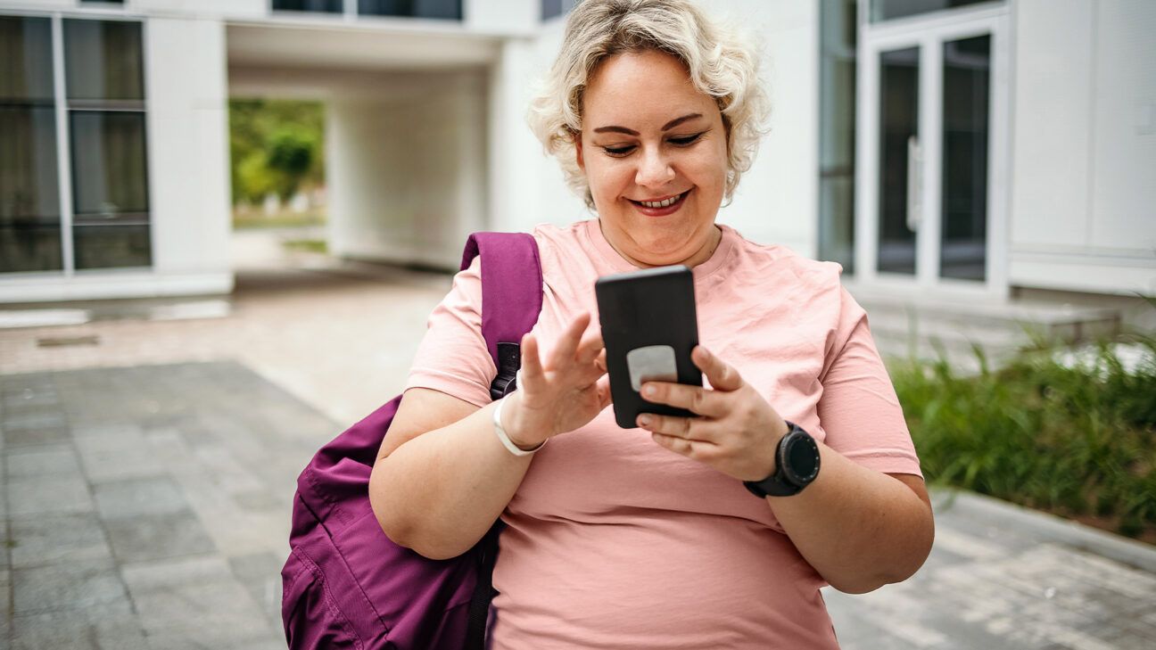 Woman in pink shirt looks at a smartphone.