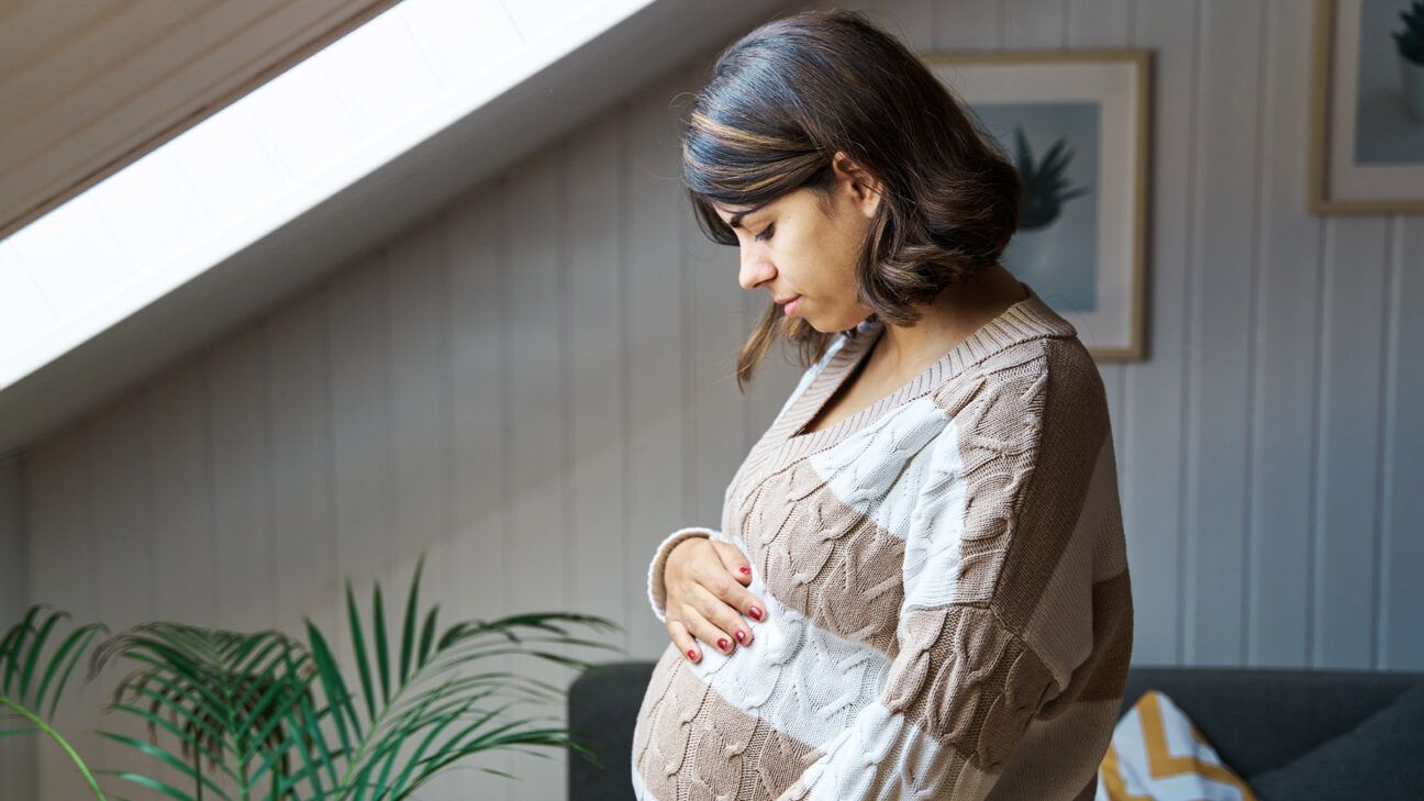 Pregnant women in striped sweater looks down.