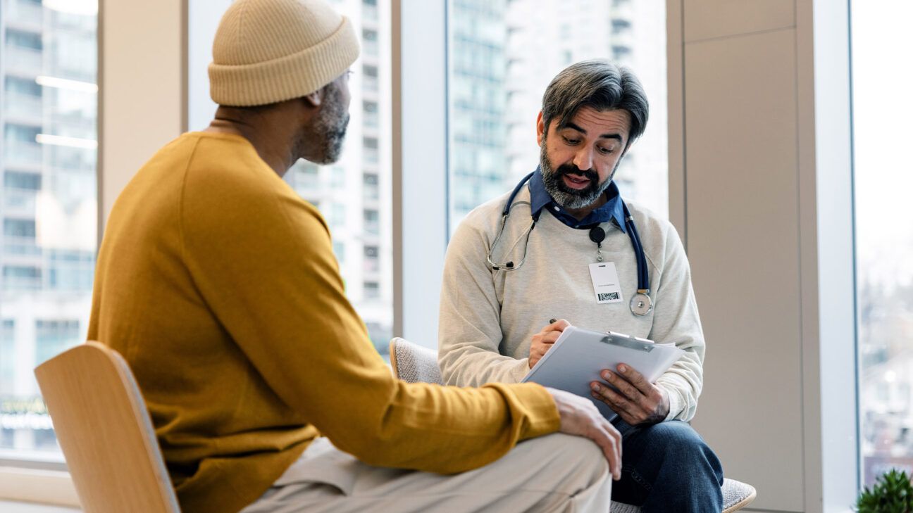  Man in yellow sweater talks to a physician in an office.