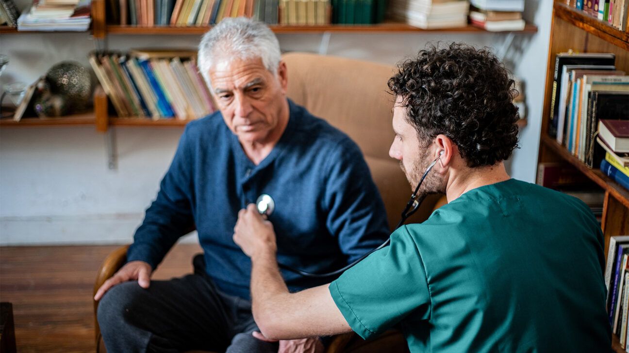 Physician talks to man with grey hair in blue sweater.