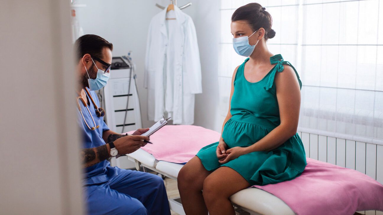 Pregnant woman in green dress sits at a physicians office.