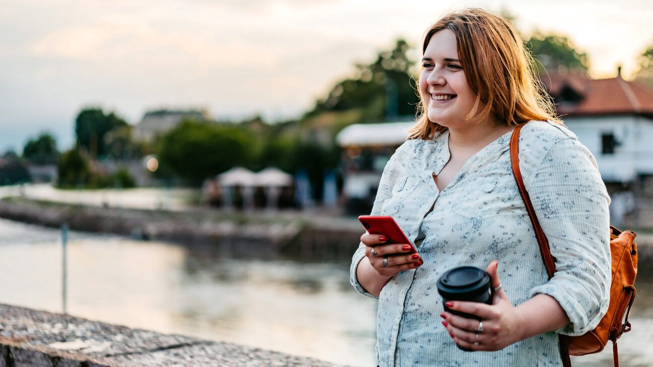 Femme tenant un téléphone et un café au bord d'une rivière