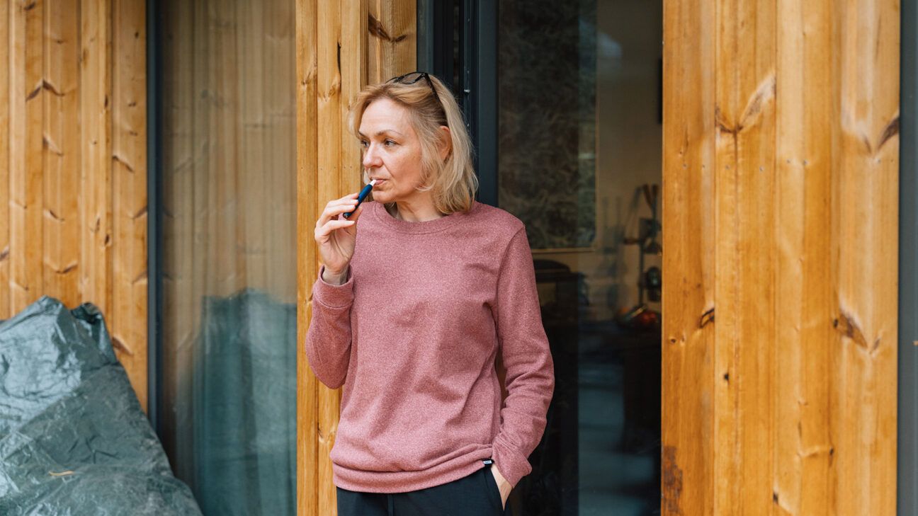 Woman in pink sweatshirt uses a vape pen.