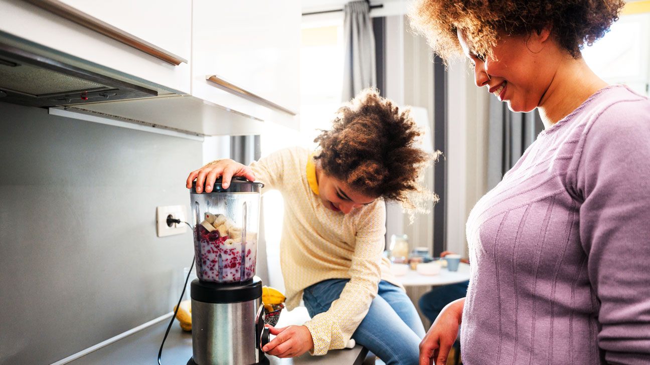 A mom and her young child make a healthy berry smoothy for breakfast.