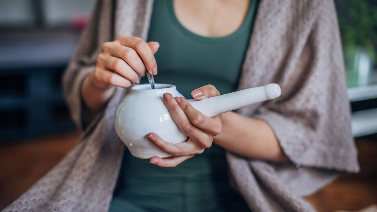 Une femme tient un dispositif d’irrigation nasale blanc.