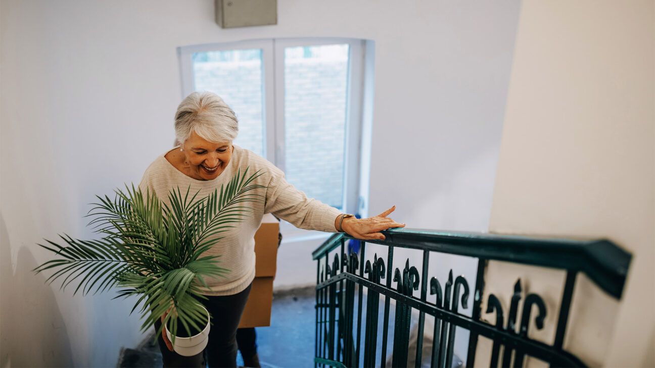 Une femme aux cheveux gris marche dans les escaliers en tenant une plante.