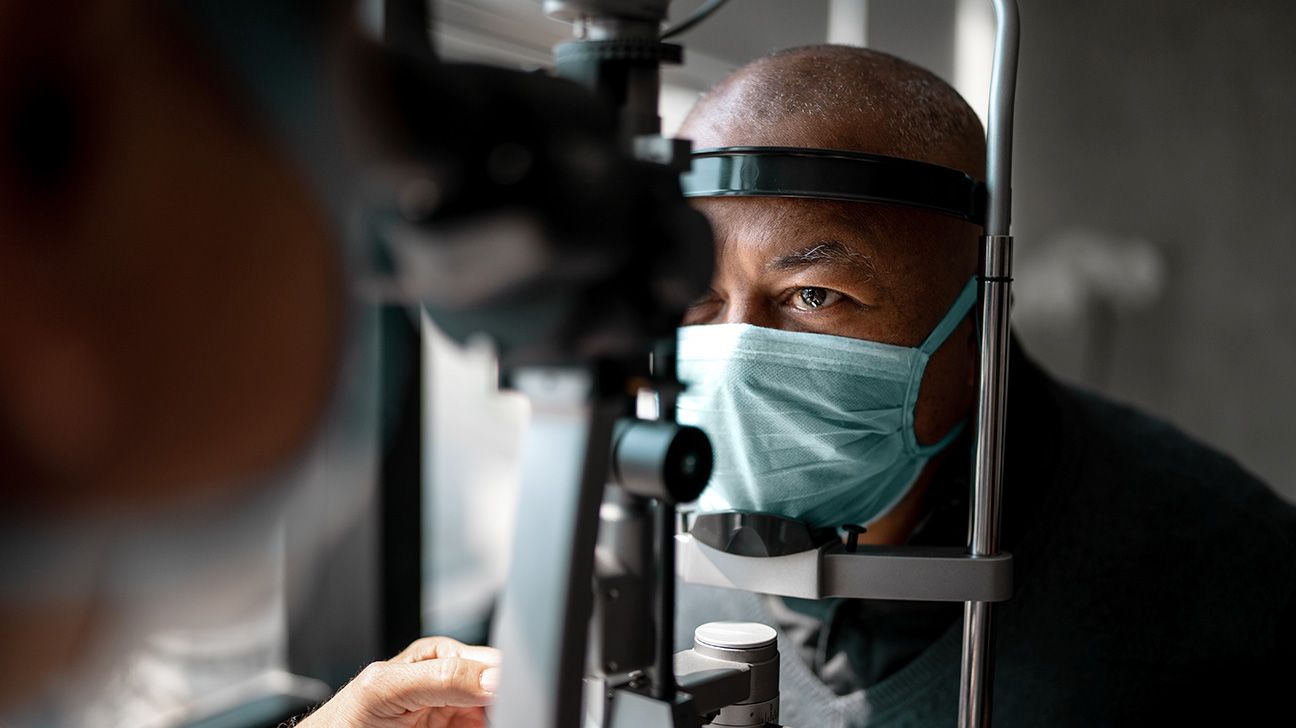 Older man wearing face mask having his vision tested with a slit lamp machine